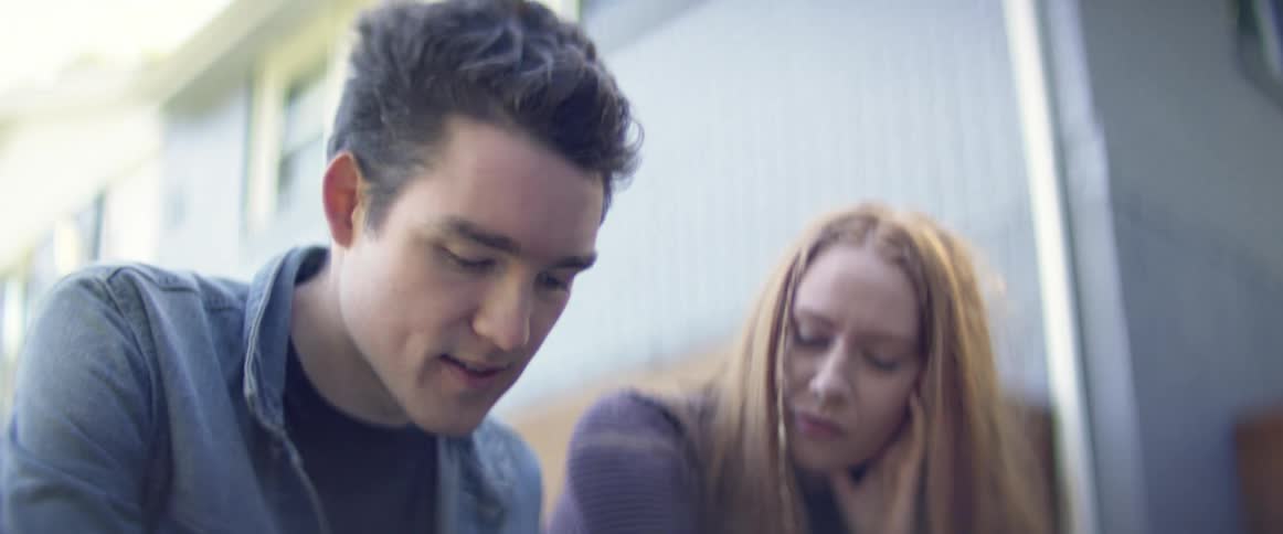 Young couple sitting outside the house looking at a phone