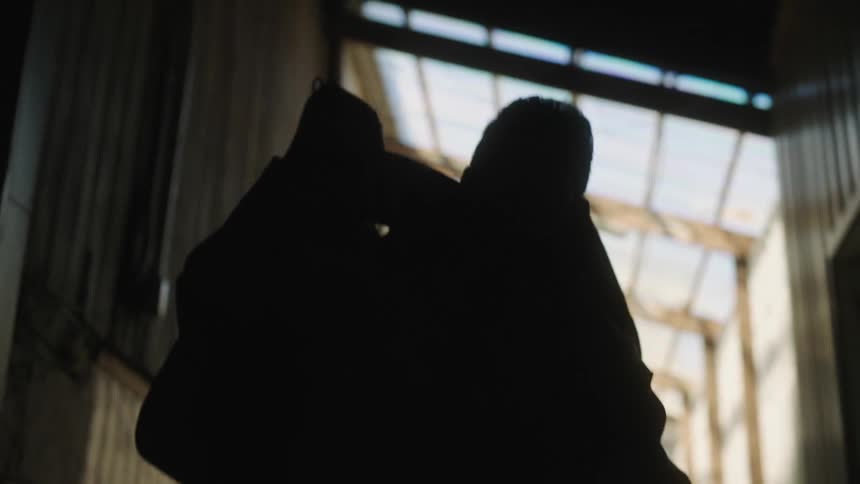 A silhouette of a man picks up a bag from off the floor inside of a building with a roof window
