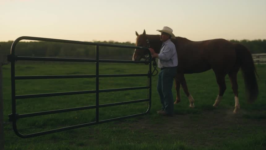 Rancher guiding a horse into a corral in a ranch at evening