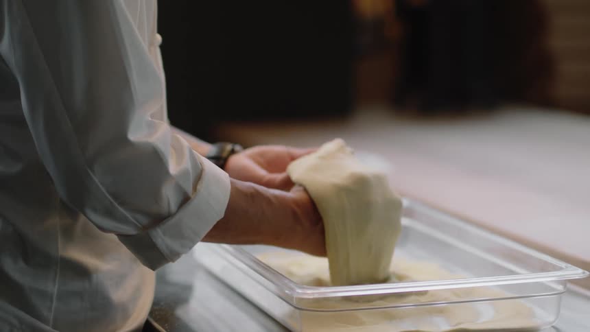 Male chef prepares dough in his hands standing at a counter