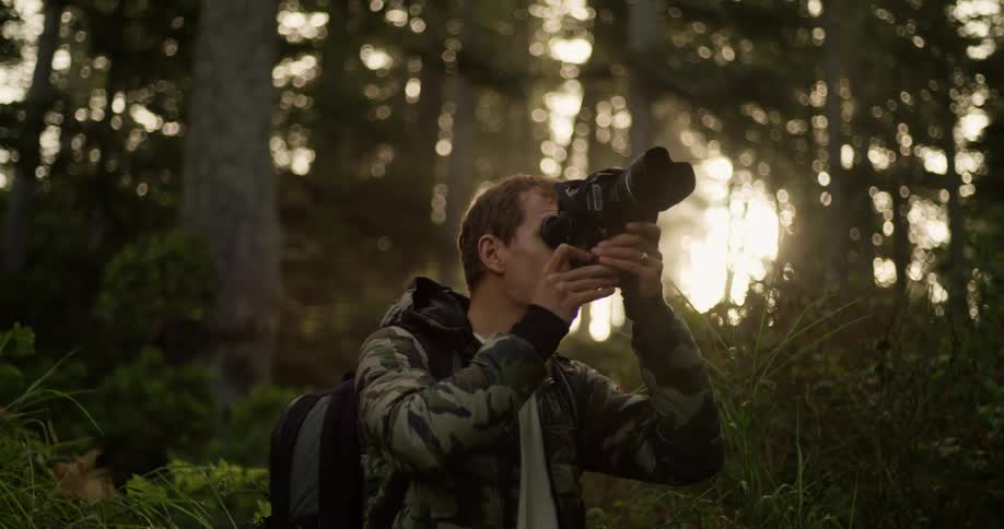 A man with a backpack and camera taking photos in the forest sunshine