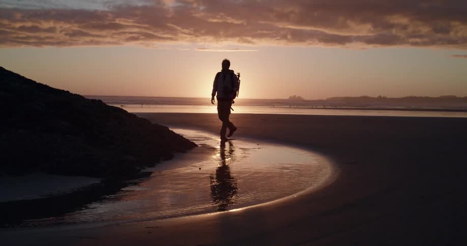A photographer climbing down from a hill walking along the sand by the beach with a camera
