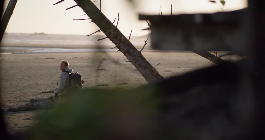 A man carrying camera walks onto the beach at sunset