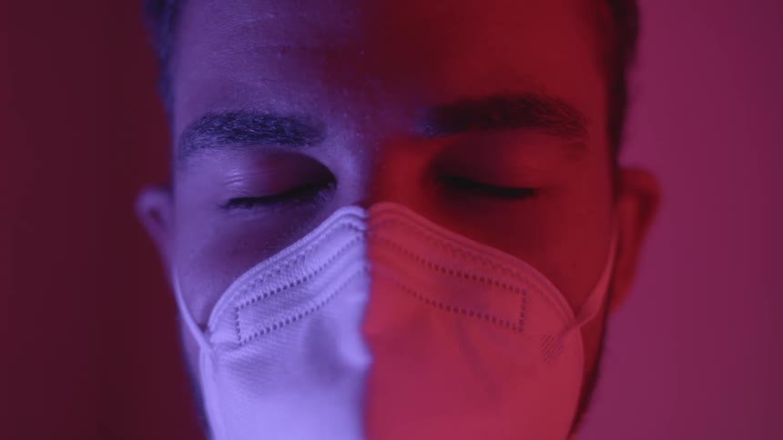 A man is standing indoors and wearing a face mask