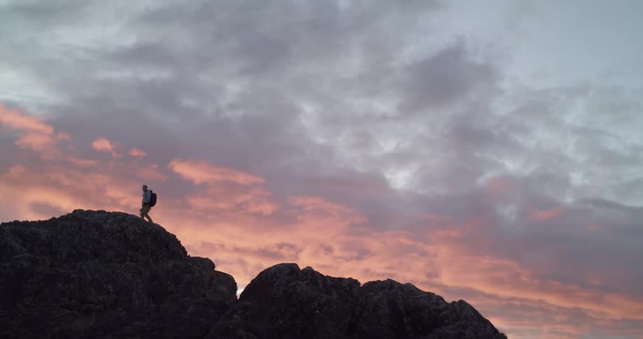 The silhouette of a person climbing to the top of some rocks under red sky