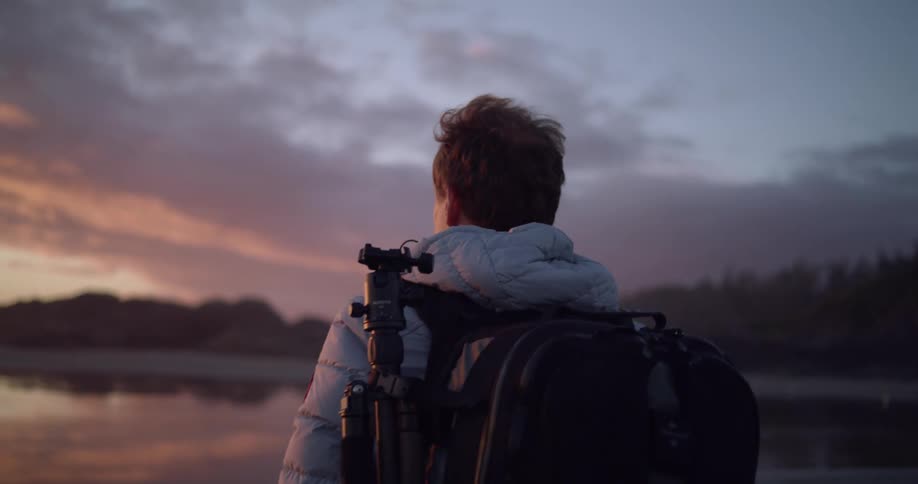 A man with backpack is watching the spring sunset on an ocean beach