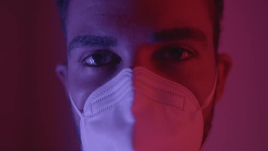 A man wearing a white surgical face mask stares off and then at the camera