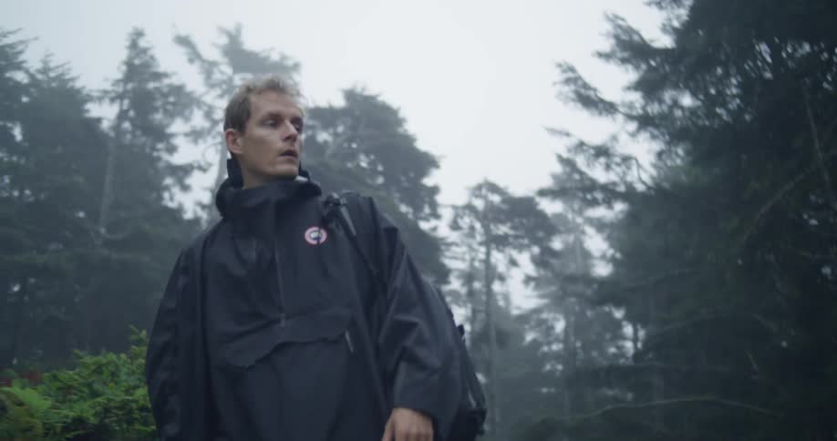 A man in rain poncho walking through a forest with backpack
