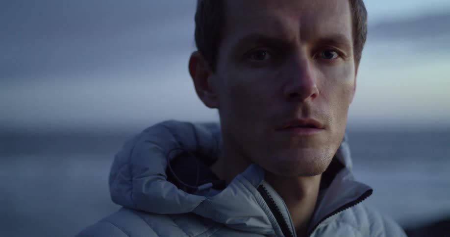Man in front of the ocean wearing a coat at dusk