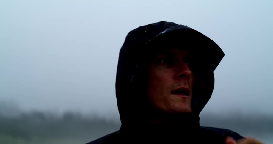 A man putting on a rain hood with foggy trees and beach in the background