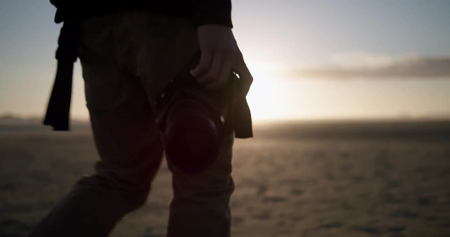 A person walking with a camera near the ocean with the sky and clouds in the background