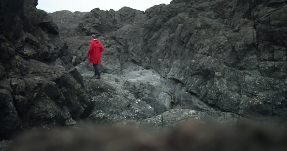 A person wearing a red jacket climbing over jagged rocks