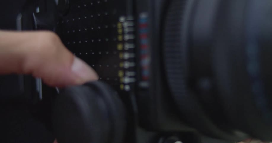 A photographer adjusting the lens of a film camera using a knob on the side