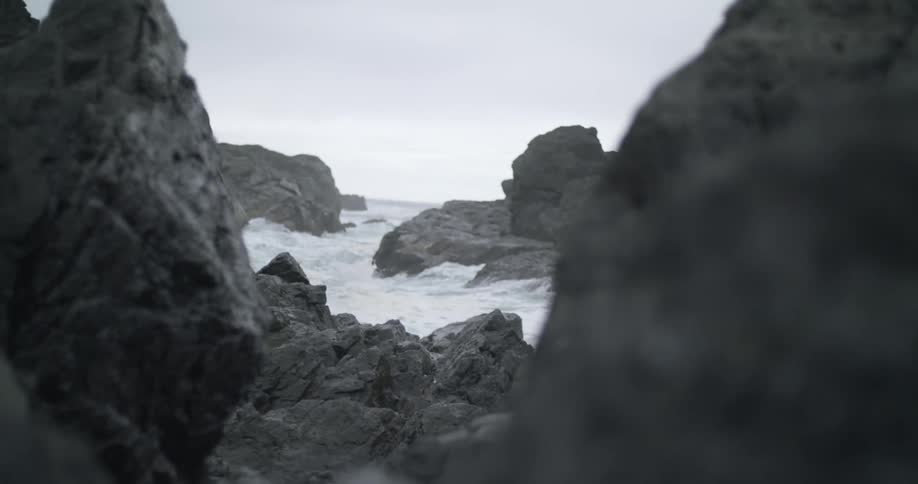 A rocky shore with waves of water crashing with the sky and clouds in the background