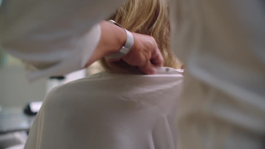 Hair stylist puts a cutting bib over a customer in the saloon