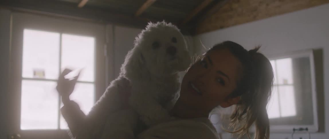 A woman in the room picking up a puppy with a mirror and a lamp in the background