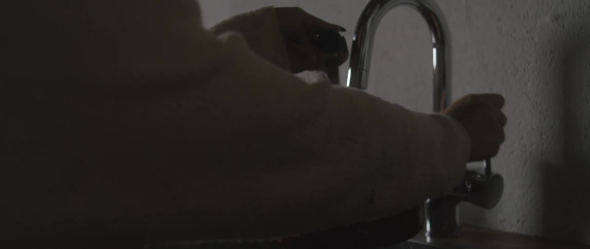 A woman turns on a kitchen sink faucet and fills a silver tea kettle