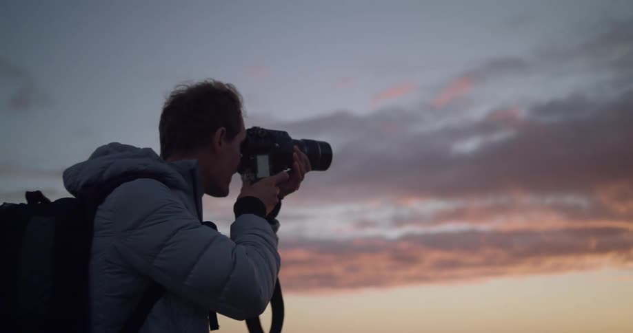 Man taking pictures of the sunset at the beach on his professional camera
