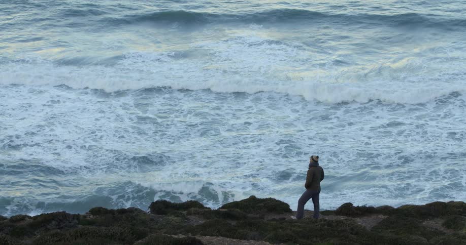 Person standing on rocky coastal bluff watching the waves roll in