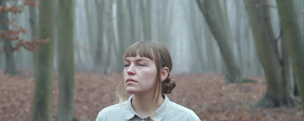 Young woman walking throught the misty woods at daytime