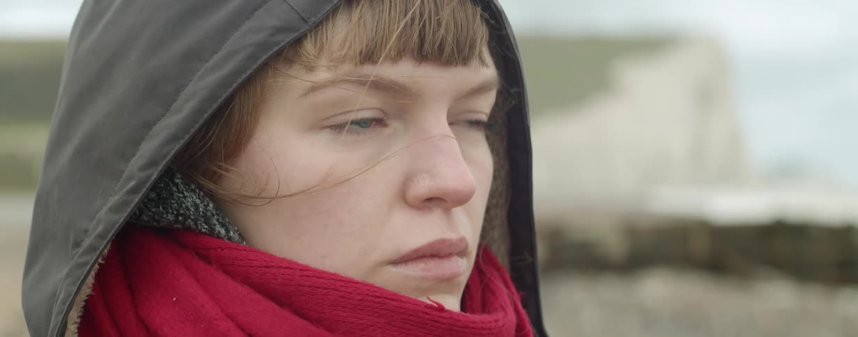 Young woman wearing a gray windbreaker and red scarf looking at the ocean