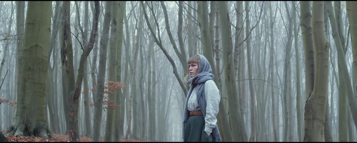 A woman stands in a forest and looks around