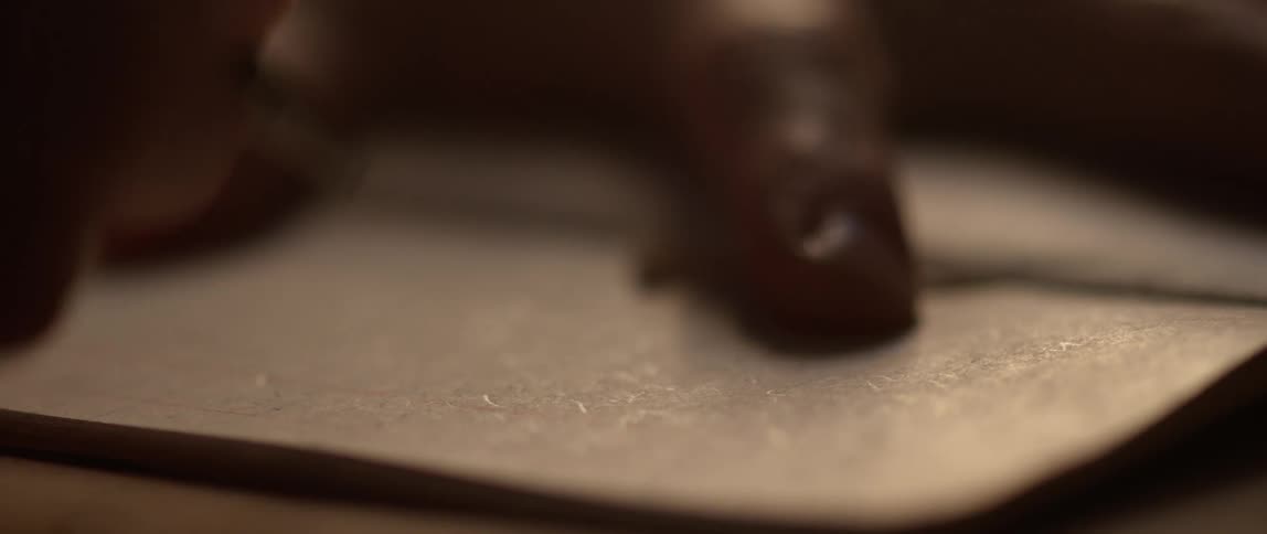 A hand holding a pen writes on a piece of paper in a small notebook