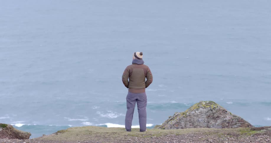 A person looking at the ocean from the top of a cliff on a windy day