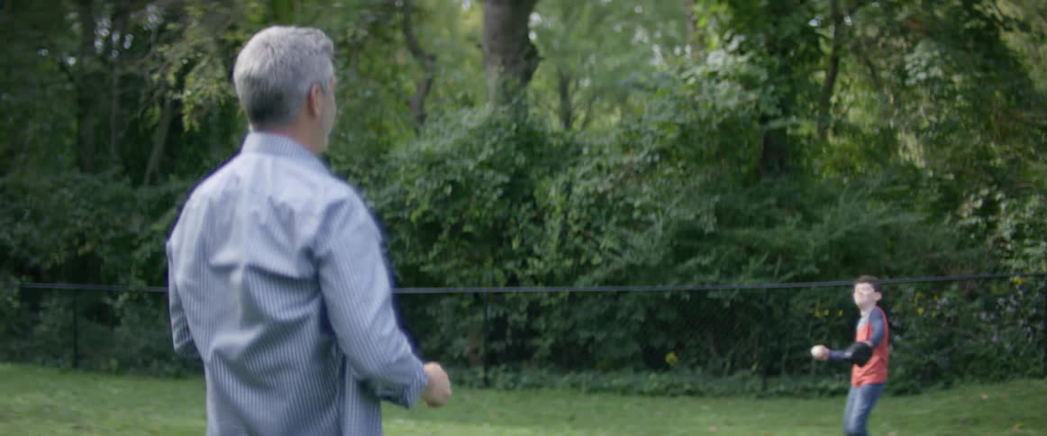 A man with gray hair plays catch with a baseball with his young son in their backyard