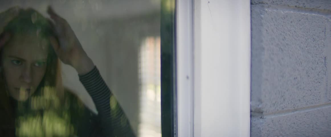 A woman nervously fixing her hair in reflection of a window