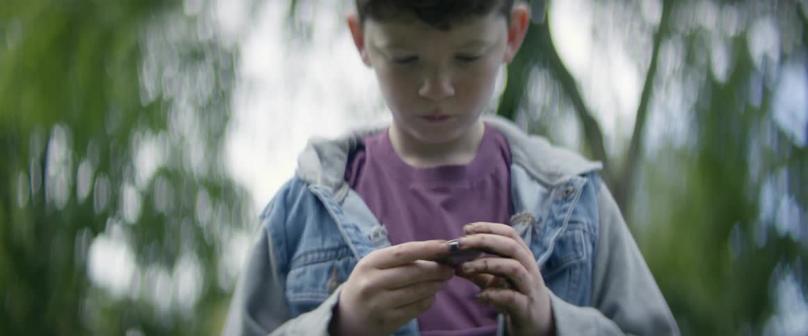 Boy stands outdoors looking at something in his hands