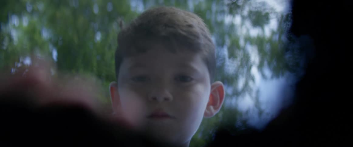 A boy digging through fallen leaves with the sky and clouds in the background