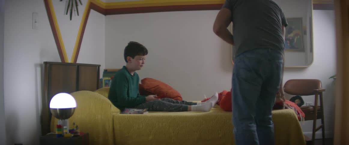 A father tucking a young boy in bed and sitting down to read a bedtime story