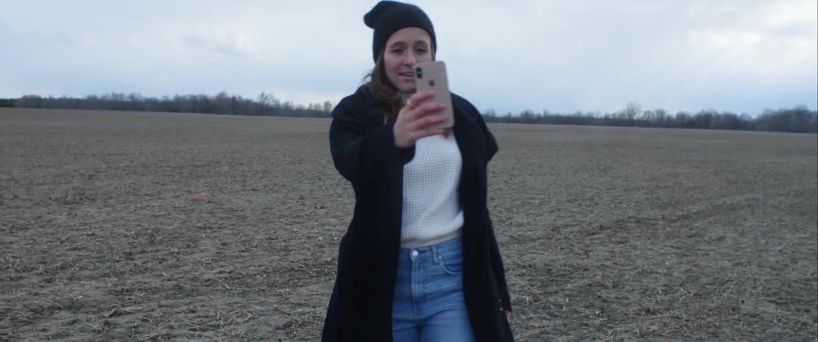 A woman moves her smartphone around during a video call to show the vast barren field shes standing in