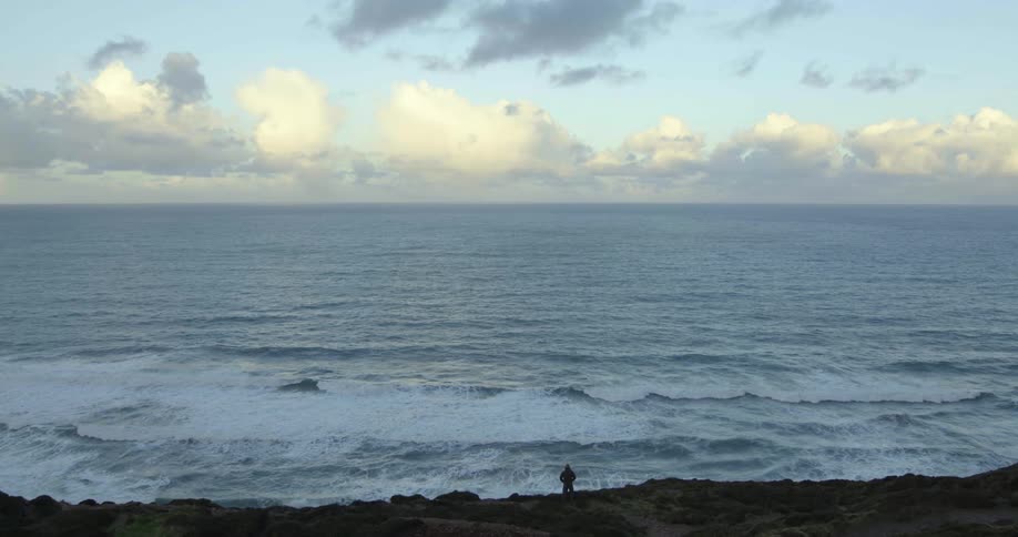 A person standing on the rocks next to the ocean at evening