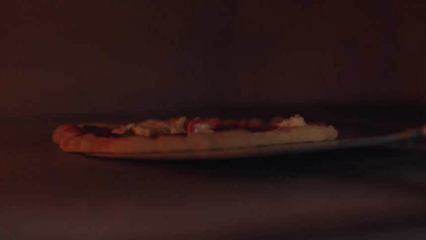 A pizza being moved in an oven