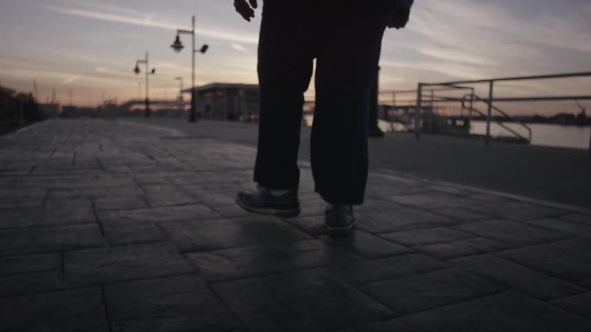 Person walking along a walkway next to waters at sunset