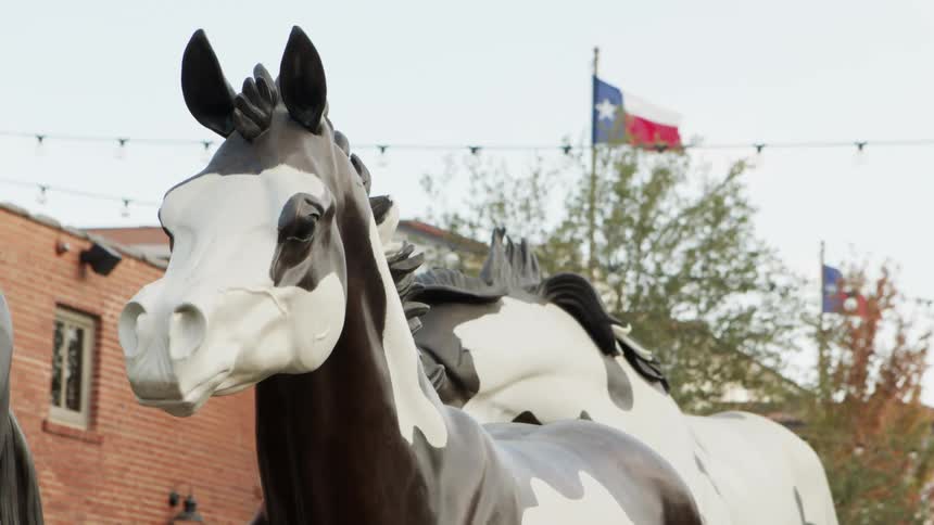 Sculpture of a herd of horses in front of waving texas flags