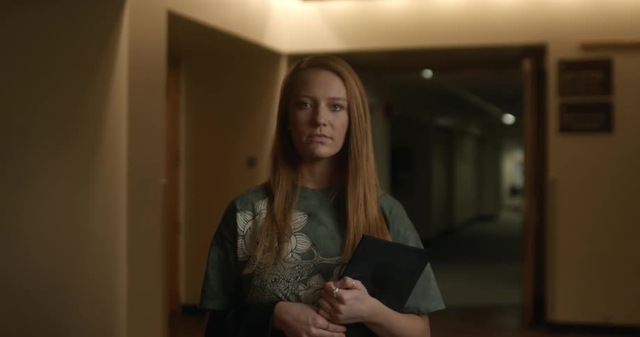Young long haired blonde woman standing in a dimly lit hallway looking at the camera