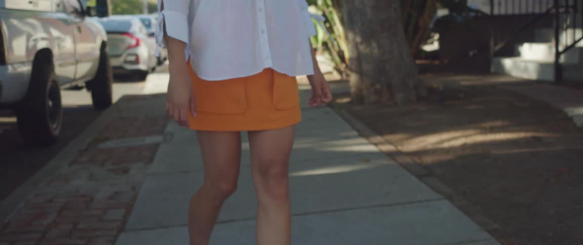 A woman in a short yellow skirt turning around to walk backwards on a sidewalk