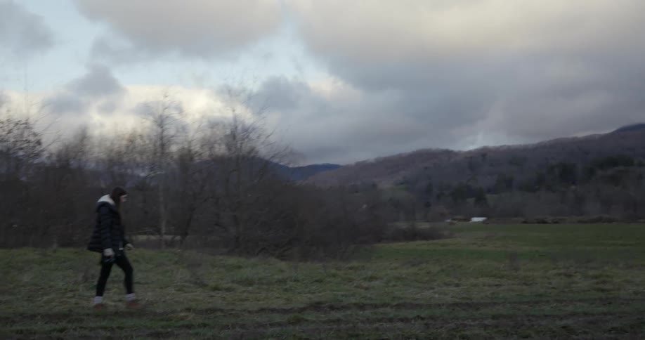 White woman wearing winter clothing walking down a grass field