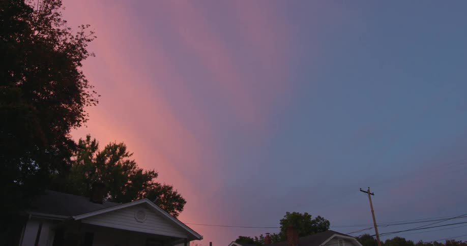 A house against a pink sky at sunset with trees and a power line