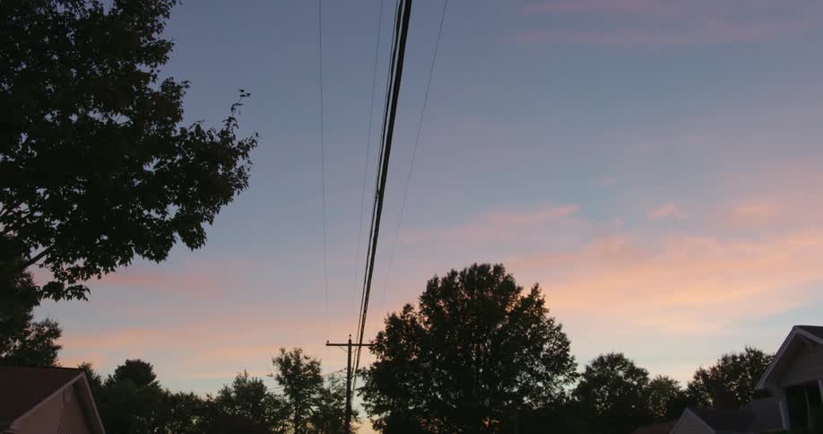 Utility pole and cables across the sky with trees and houses around