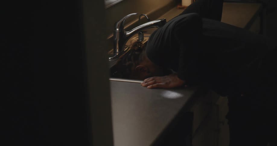 Young man submerging his face in the water on the kitchen sink at home