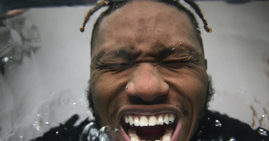 A man dipping his head in water and blowing bubbles