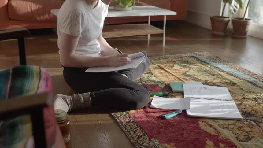 Woman sitting in the floor on the livingroom taking notes on a notebook studying