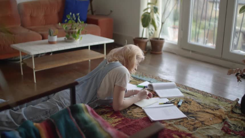 A teenager lies on the floor at home and does homework