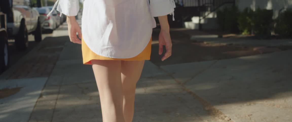 Young woman in a yellow mini skirt walking on the sidewalk at daytime