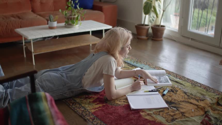 Female writing in book while lying down on floor