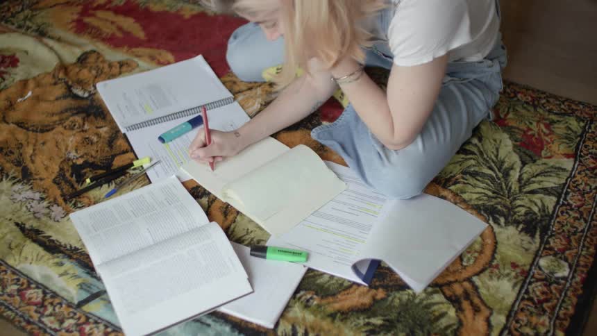 Teenager girl sitting down on her carpet at living room and studying with her books and notebooks